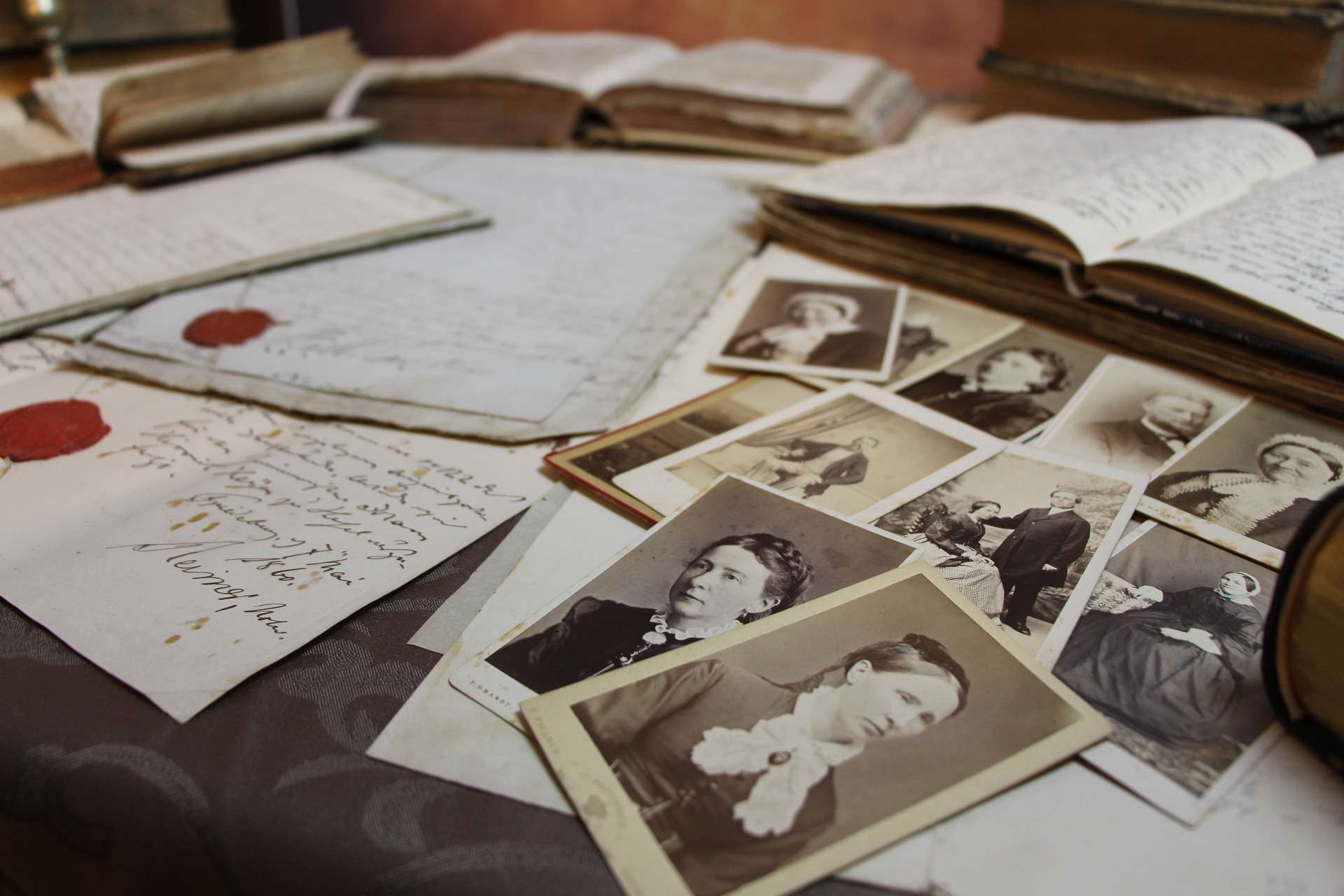 table covered by old handwritten letters with red wax seals, open books, and rows of vintage photographs of ladies and couples